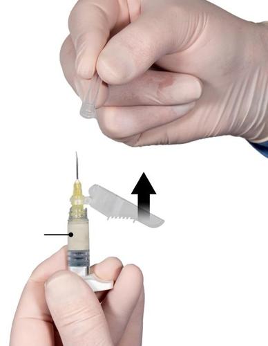 Mano con guanto che tiene una siringa e un ago, con freccia che indica la direzione di inserimento e dettaglio del meccanismo di sicurezza
