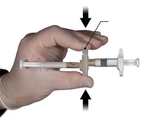 Mano con guanto che tiene una siringa preriempita con ago protetto da cappuccio e frecce nere che indicano la direzione di attivazione