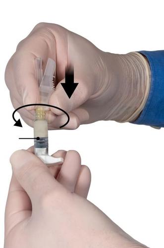 Mano con guanto che ruota un adattatore per siringa collegando una fiala di farmaco a una siringa preriempita freccia nera indica la rotazione