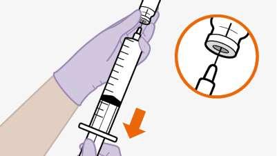 Siringa con ago e guaina protettiva, mano guantata che tiene la siringa e freccia arancione che indica la direzione di inserimento