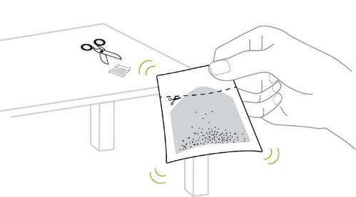Mano che apre una bustina contenente granuli, con forbici e bustina vuota accanto su una superficie chiara