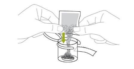 Mani che aprono una bustina sopra un cilindro trasparente con polvere scura che vi cade dentro freccia verde indica la direzione