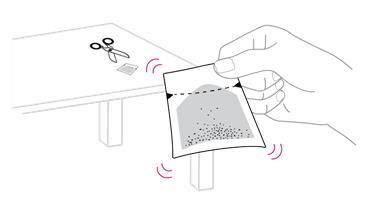 Mano che apre una bustina contenente granuli, con forbici e bustina vuota accanto su una superficie chiara