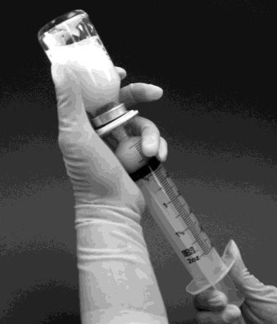 Mano con guanto che tiene una siringa piena e un flacone medicinale con tappo metallico e gomma