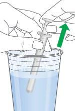 Siringa immersa in un bicchiere con liquido trasparente, freccia verde indica direzione di aspirazione del farmaco