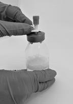 Mano con guanto che tiene e ruota il tappo di un flacone di vetro trasparente con liquido medicinale all