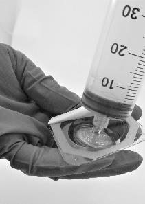 Siringa graduata con liquido trasparente che riempie un adattatore grigio per infusione sottocutanea tenuto da una mano guantata