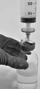 Mano con guanto che tiene una siringa collegata a un flacone di medicinale tramite un adattatore bianco e nero