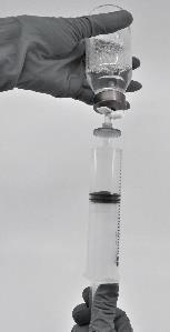 Mano con guanto che tiene una siringa collegata a una fiala trasparente contenente liquido medicinale