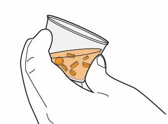 Mano che tiene un bicchiere contenente una miscela di capsule e compresse di colore arancione