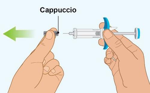 Mano che rimuove il cappuccio protettivo da una siringa preriempita con ago blu e corpo trasparente freccia verde indica la direzione