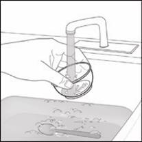 Mano che versa acqua da un rubinetto in un bicchiere sopra un lavello con un cucchiaino visibile