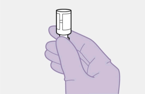 Mano con guanto viola che tiene un dispositivo medico cilindrico bianco con parte superiore argentata e finestra trasparente