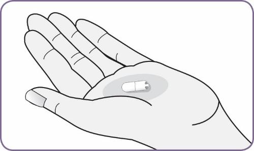 Mano aperta che mostra una capsula bianca ovale al centro del palmo su sfondo grigio chiaro