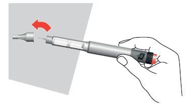 Penna per iniezione con ago esposto e freccia rossa che indica la rotazione del dispositivo tenuto in mano