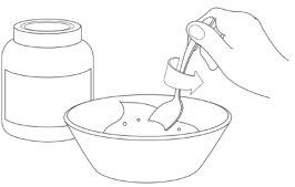Hand holding a dropper dripping liquid into a white container with a removed lid and a cylindrical bottle next to it